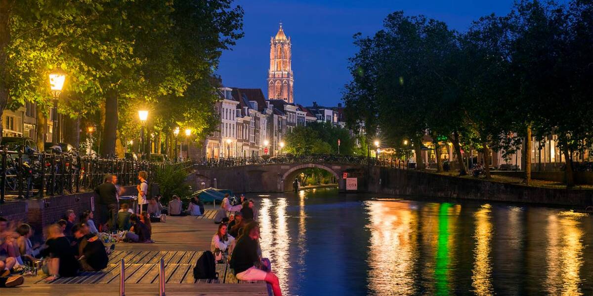 Link naar foto in Flickr: mensen zitten in de avond langs het water met op de achtergrond een verlichte Dom. 