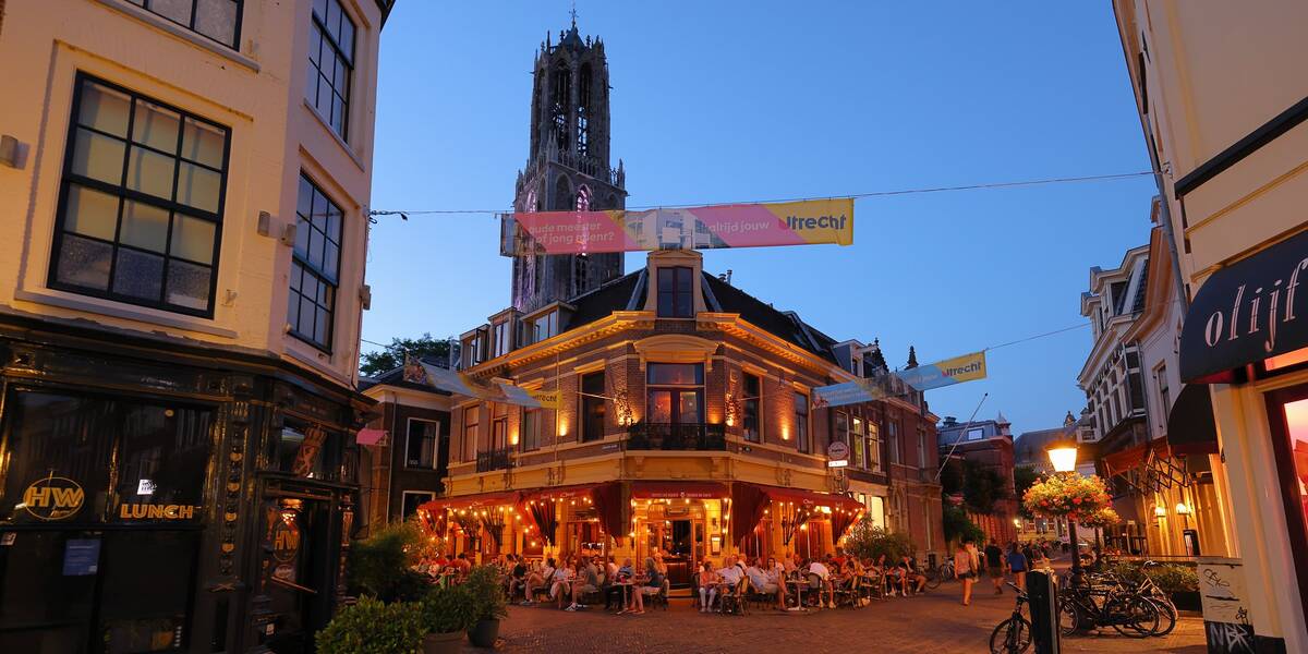 Link naar foto in Flickr: mensen zitten in de avond op het terras op 't Wed. Op de achtergrond gloort de Dom.