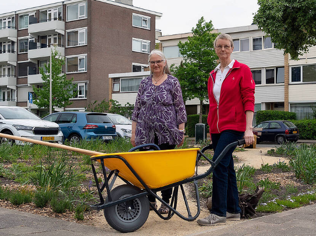 2 mensen met een kruiwagen staan voor de buurttuin.