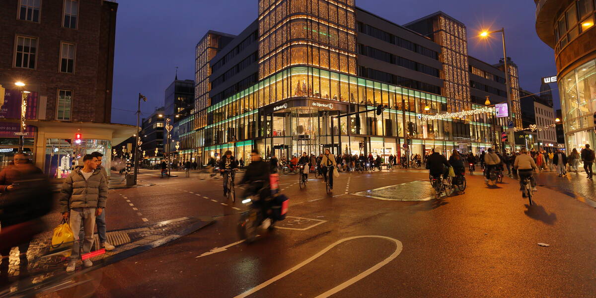 Link naar foto in Flickr: mensen steken over bij Vredenburg bij de stoplichten bij de Bijenkorf in de avond. 