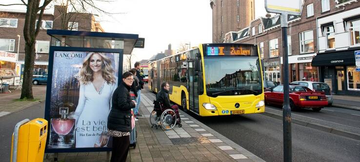 Verschillende mensen, waaronder een met een rolstoel, wachten bij bushalte