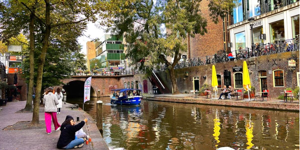 Link naar foto in Flickr: mensen zitten en wandelen langs de nieuwegracht ter hoogte van de Viebrug. In de gracht een blauwe boot.