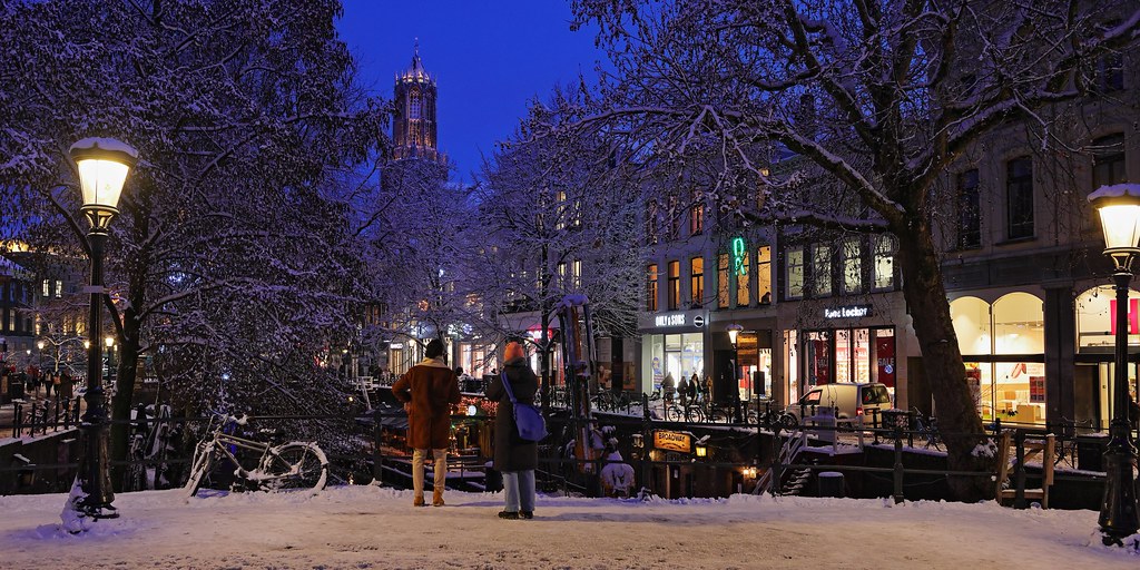 Link naar foto in Flickr: 2 mensen staan op een besneeuwde Bakkerbrug, op de achtergrond de Dom.